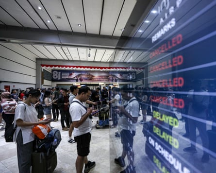 Passengers stand in front of a large screen displaying details of cancelled and delayed flights
