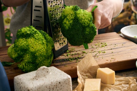 A box grater being used to grate a head of broccoli. 