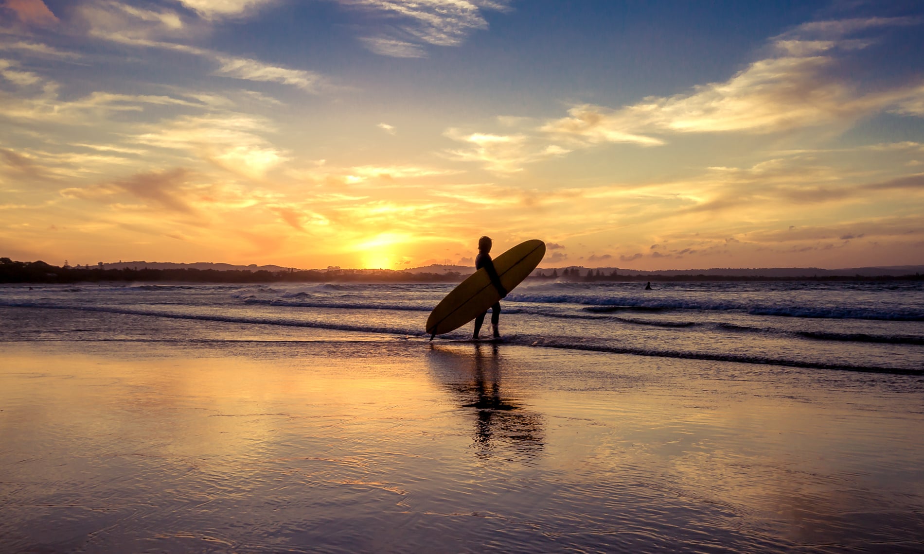 A person with a surfboard at sunset