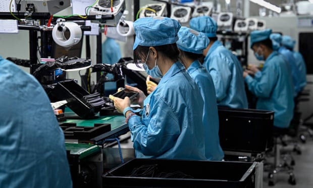Employees in blue gowns and masks working on a smartphone assembly line in a factory in southern China