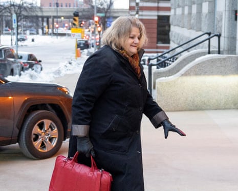 a woman in a black coat and carrying a red handbag walks on a sidewalk as another woman and man walk behind her