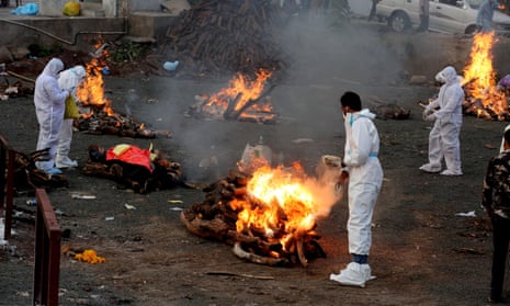 Relatives wear protective equipment amid burning funeral pyres for Covid-19 victims in India.