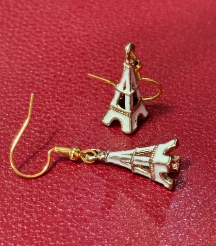 A pair of mini white enamel Eiffel Tower drop earrings for pierced ears on a red leather background