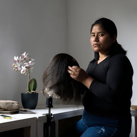 An Indigenous woman in jeans sits at a worktop with a wig on a mould