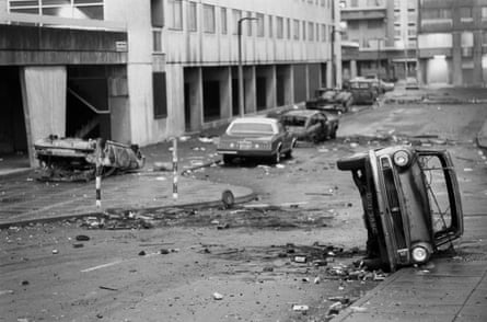 Black and white photo of a street on a neglected estate littered with burnt-out cars