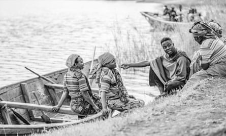 Les pêcheuses sont assises dans un bateau et aussi sur la berge, parlant à Makembe.  Tous portent des vêtements traditionnels