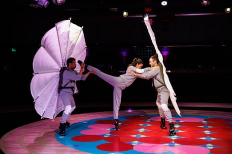 Three people dance together while holding each other up in a skating rink