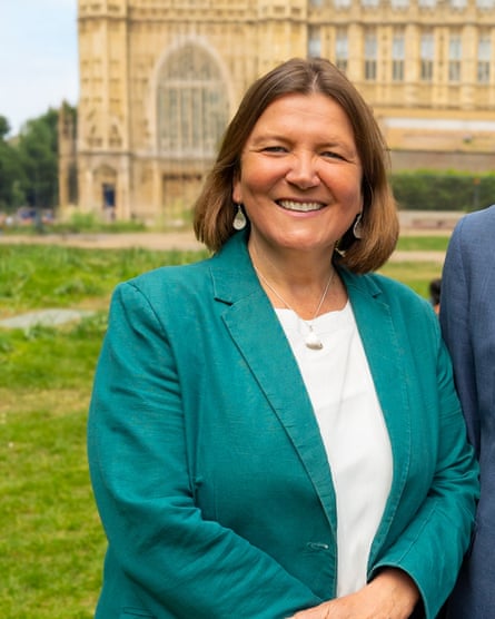 Ellie Chowns stands in front of a cathedral or large church. She wears a green jacket and white blouse, and is smiling.