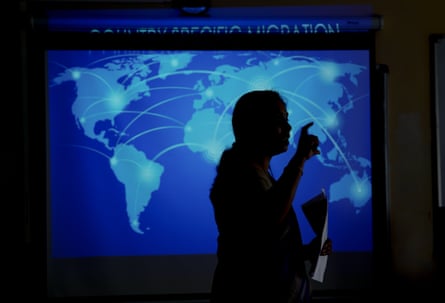 A woman can be seen in outline in front of a map of the world with arrows on it.