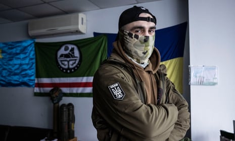 Volunteer Maga poses for a photo in front of the Crimean (left), Chechen (centre) and Ukrainian flags in the Dzhokhar Dudayev battalion base in Kyiv