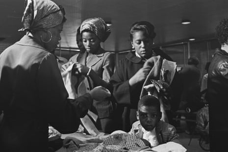 A young boy stares at the camera while members of the Black Panther Party distribute free clothing to the public.