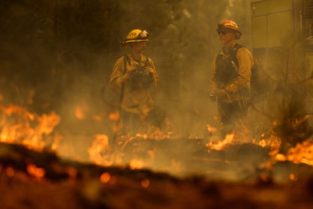 two firefighters stand around flames on ground