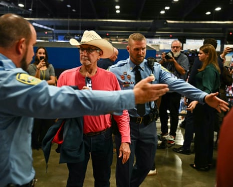 Police escort a protestor wearing a cowboy hat out of a crowded campaign rally venue