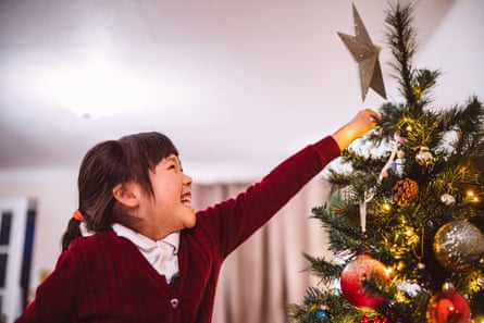 Cheerful young girl decorating a Christmas tree with a star topper at home during a festive holiday