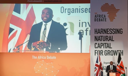 David Lammy speaks at a lectern in front of a large poster for the Africa Debate. Next to him he is being streamed on a large screen
