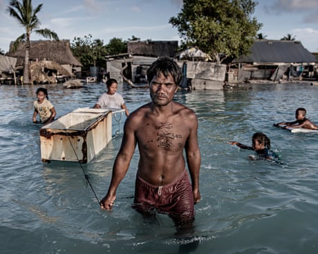 A family wading through sea water flooding a village