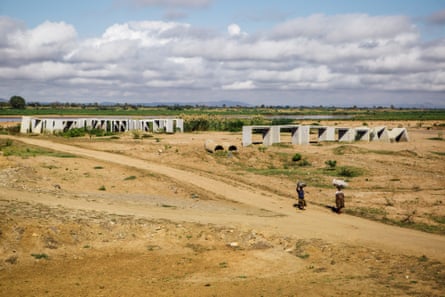 Two women walk across dry land with bags on their heads.