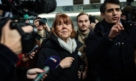 Gisèle Pelicot, with a scarf tucked into her jacket, smiles surrounded by photographers