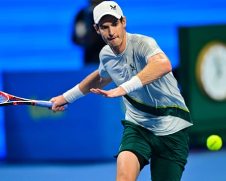 Andy Murray wearing a baseball cap and green shorts prepares to hit a forehand