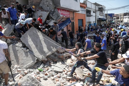 People use ropes to try to pull up a large piece of a collapsed building in an area of earthquake damage
