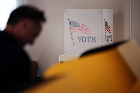A man sits at a voting booth decorated with American flags and "VOTE" text