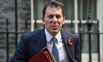Close up of John Glen wearing a suit with a remembrance poppy holding a red folder