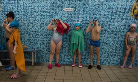 A group of small children in their swimming costumes put on their goggles by the pool