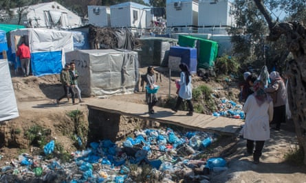 People cross a bridge over bags of waste in the Moria camp in May