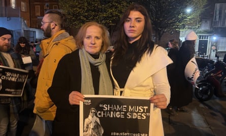 Two women hold a placard that says Shame Must Change Sides