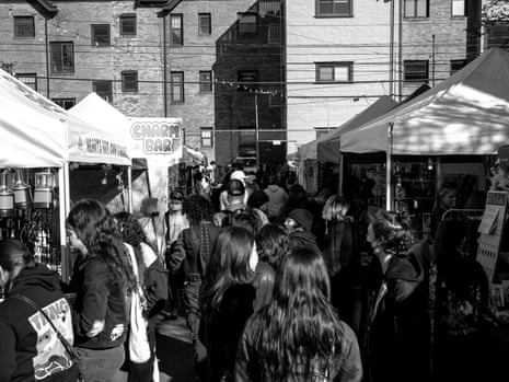 A black-and-white image of people walking and shopping between two rows of pop-up tents.