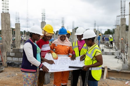 A group of female workers in hard hats look at construction plans on a building site