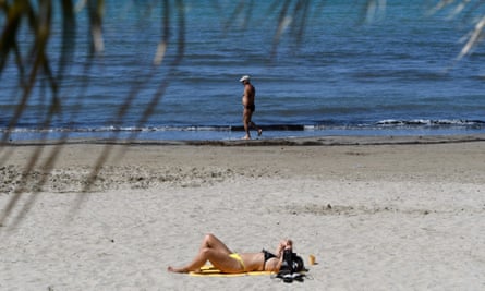 woman sunbathing on beach with man standing in shallow sea
