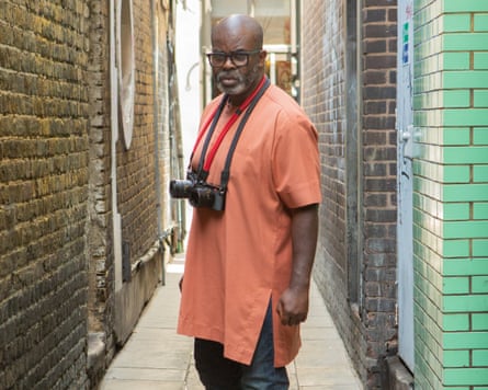 Misan Harriman stands in a London alleyway, two cameras around his neck