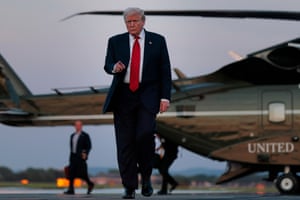 Donald Trump walks towards the camera pointing, as a helicopter sits on the tarmac behind