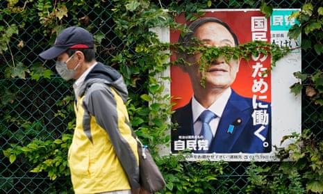 A man wearing a face mask walks past a poster of outgoing Japanese prime minister Yoshihide Suga