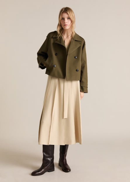 A model wearing an olive green cropped trench coat and cream skirt