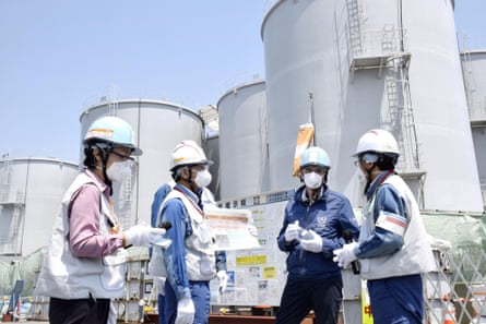 Four men in hard hats and masks stand in front of huge metal tanks
