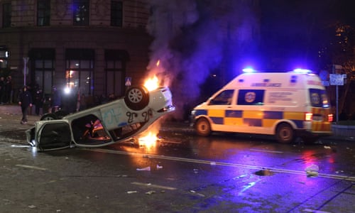 An ambulance drives past an overturned car set on fire during a protest in Tbilisi.