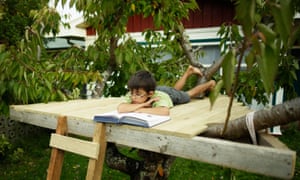 A boy reading a book in a treehouse.