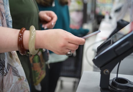 Close-up of a hand with jade and brown bracelets inserting a credit card into a payment terminal at a store checkout.
