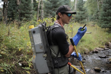 Michael Miller stands in a stream, carrying scientific equipment and speaking into a walkie-talkie.