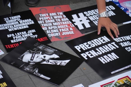 A hand touches posters spread out on the ground or a table