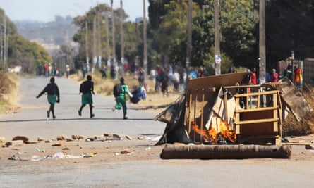 Schoolchildren run past a burning barricade in Harare