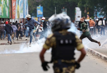 A member of the security forces looks on as protesters leap over cloud of smoke or gas.