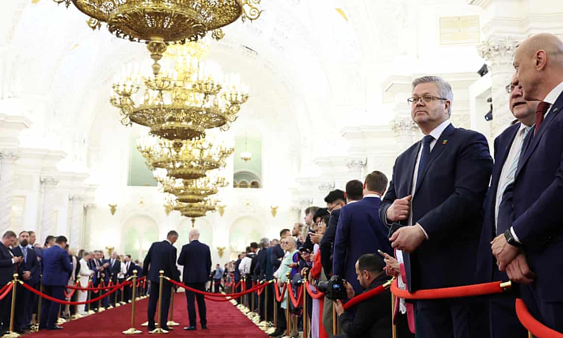 People in suits stand at the side of a red carpet