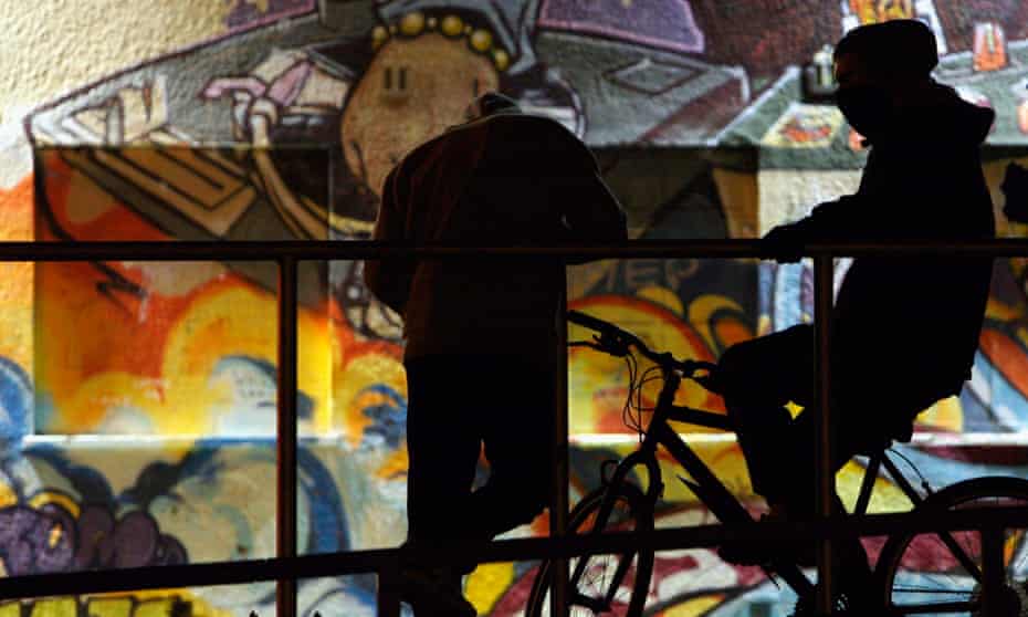 Two boys with bikes, hang around in front of a graffiti wall