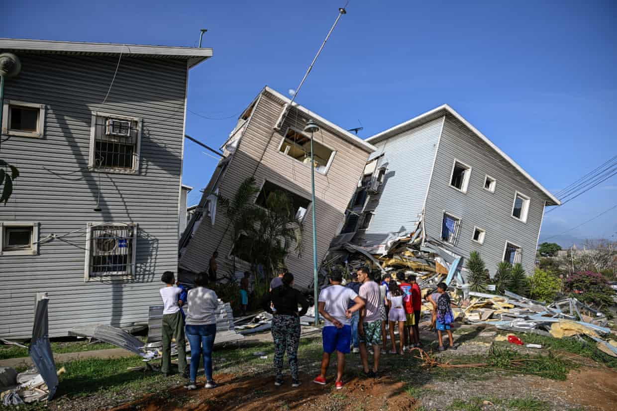 People stand outside homes that are tilted sideways