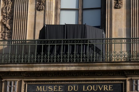 it is placed on the balcony covering the broken glass. Gold lettering reading Musee du Louvre is seen under the balcony over a doorway.