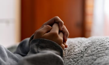 Close-up of clasped hands of young adolescent lying in bed, indicating anxiety and nervousness, with closed door behind