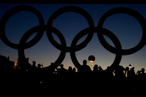 People watch the cauldron rise at sunset near to the Olympic rings.